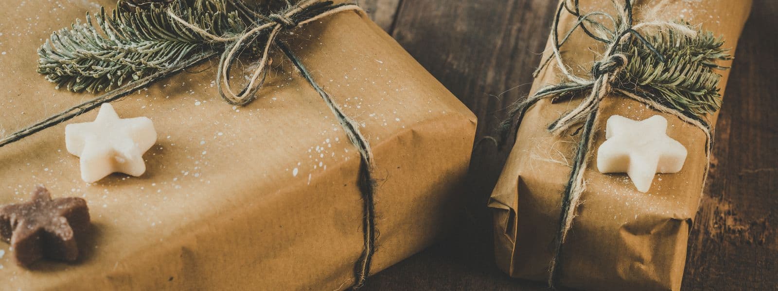 Two presents wrapped in brown kraft paper and tied with twine and pine sprigs on a wooden table