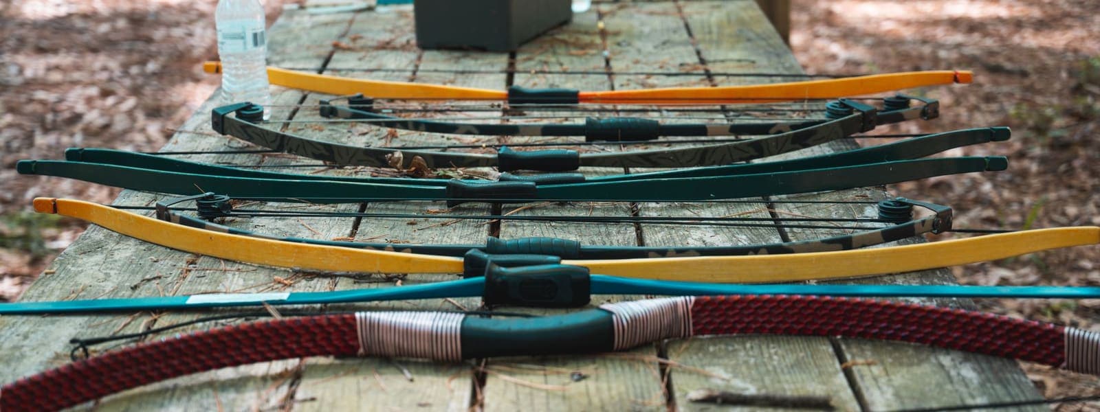 Bows and arrows laid out on a wooden table at the edge of the woods, the way a kit gets assembled before a first season